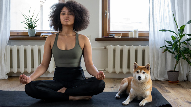 Woman sitting with her dog on a yoga mat and doing a butterfly yoga pose